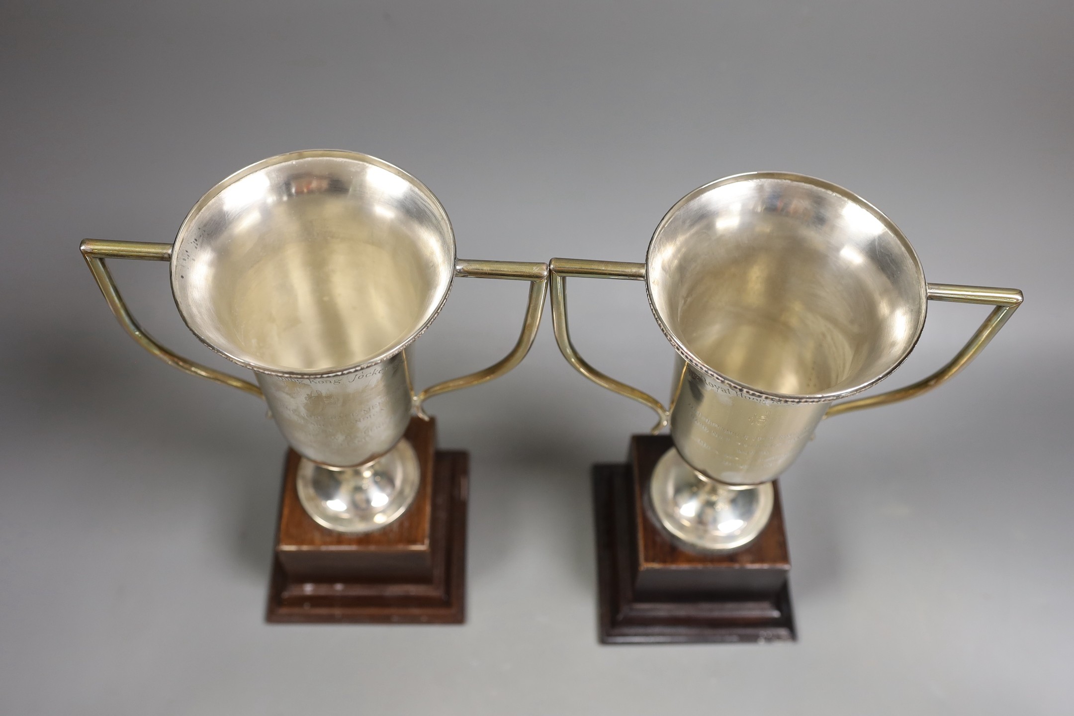 A pair of Royal Hong Kong Jockey Club sterling presentation two handled trophy cups and covers, fixed to wooden plinth bases, height of cups 26cm.